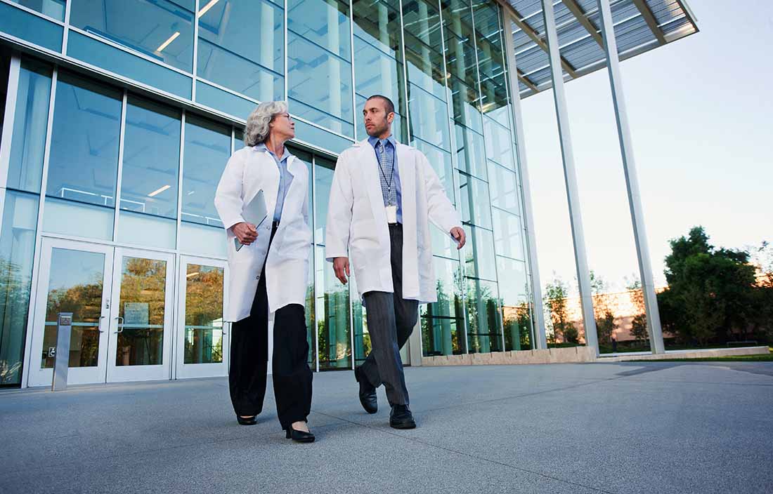 Two doctors walking together outside of a modern hospital.