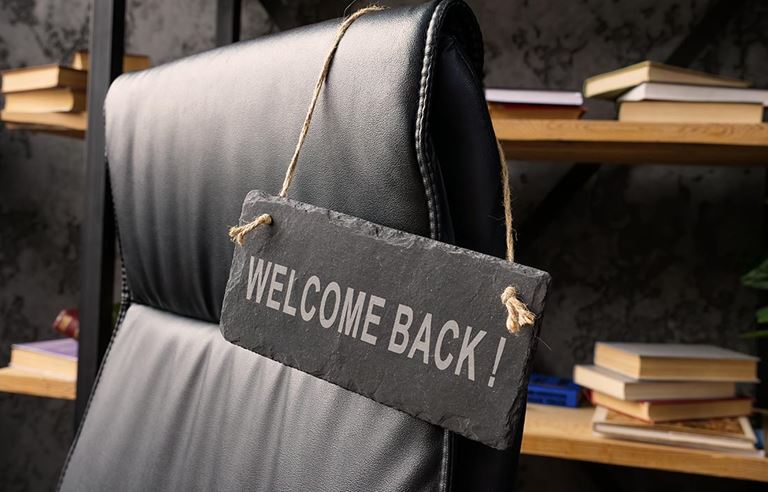Computer hair in a dark office with Welcome Back sign